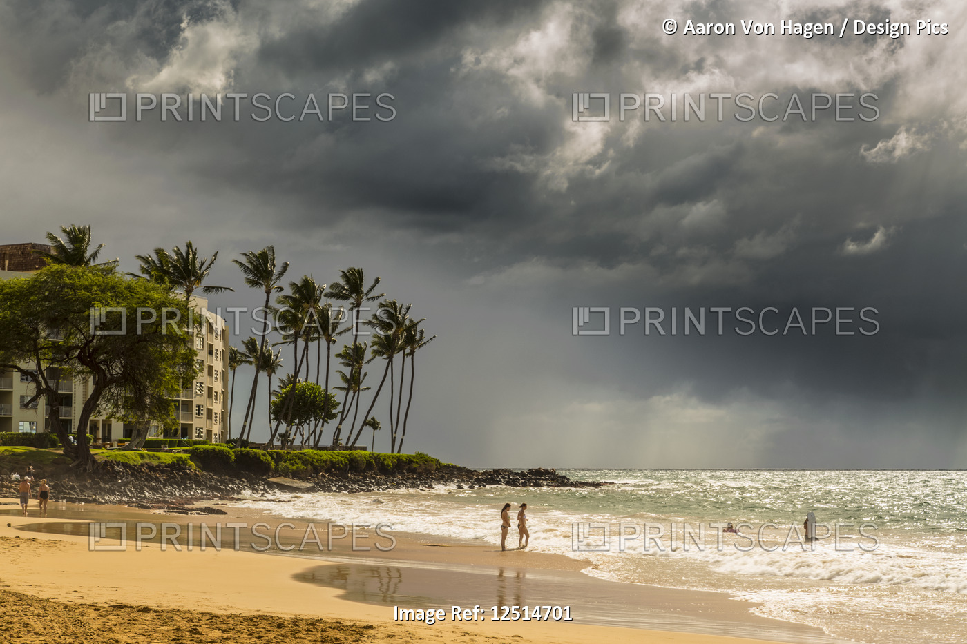Tourists on a beach on the island of Maui with dark clouds and rainfall over ...