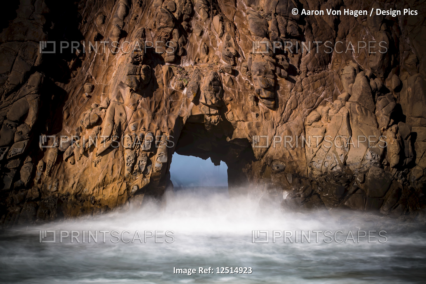 A natural arch in the rock formation along the coast with mist rising off the ...