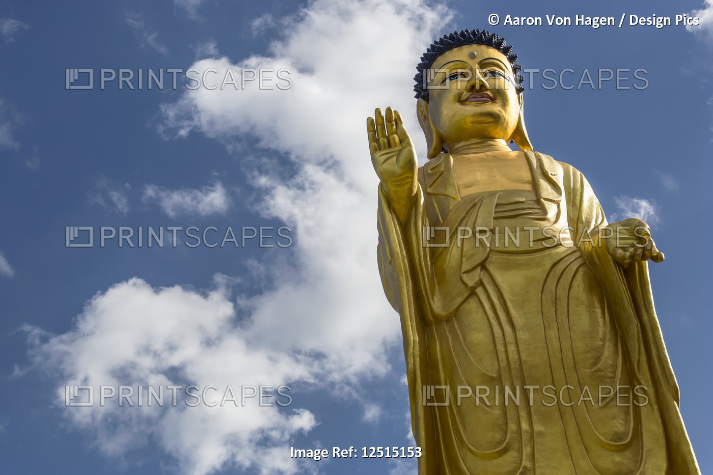 Low angle view of a gold Buddha statue against a blue sky with cloud; ...