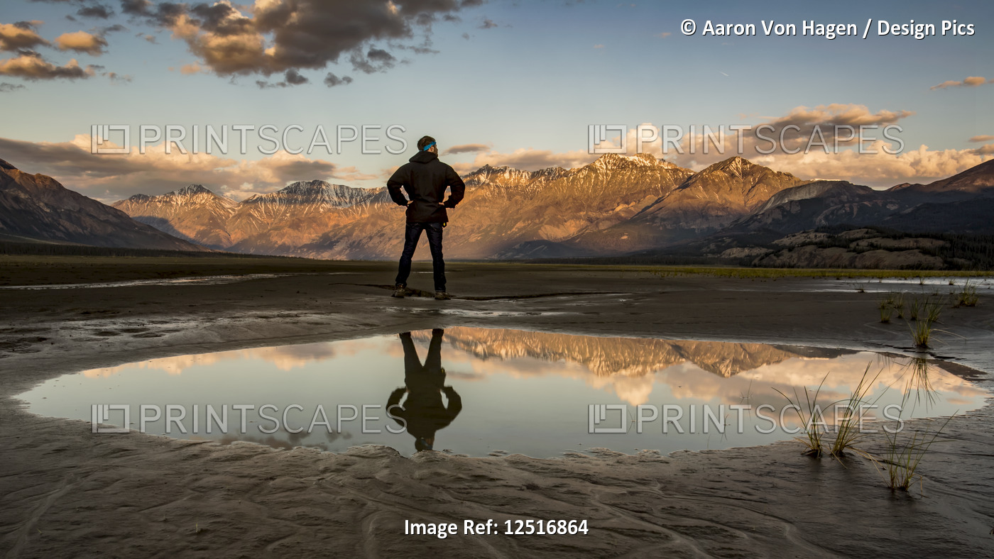 A man stands with his reflection in a pool of water looking out over the Saint ...
