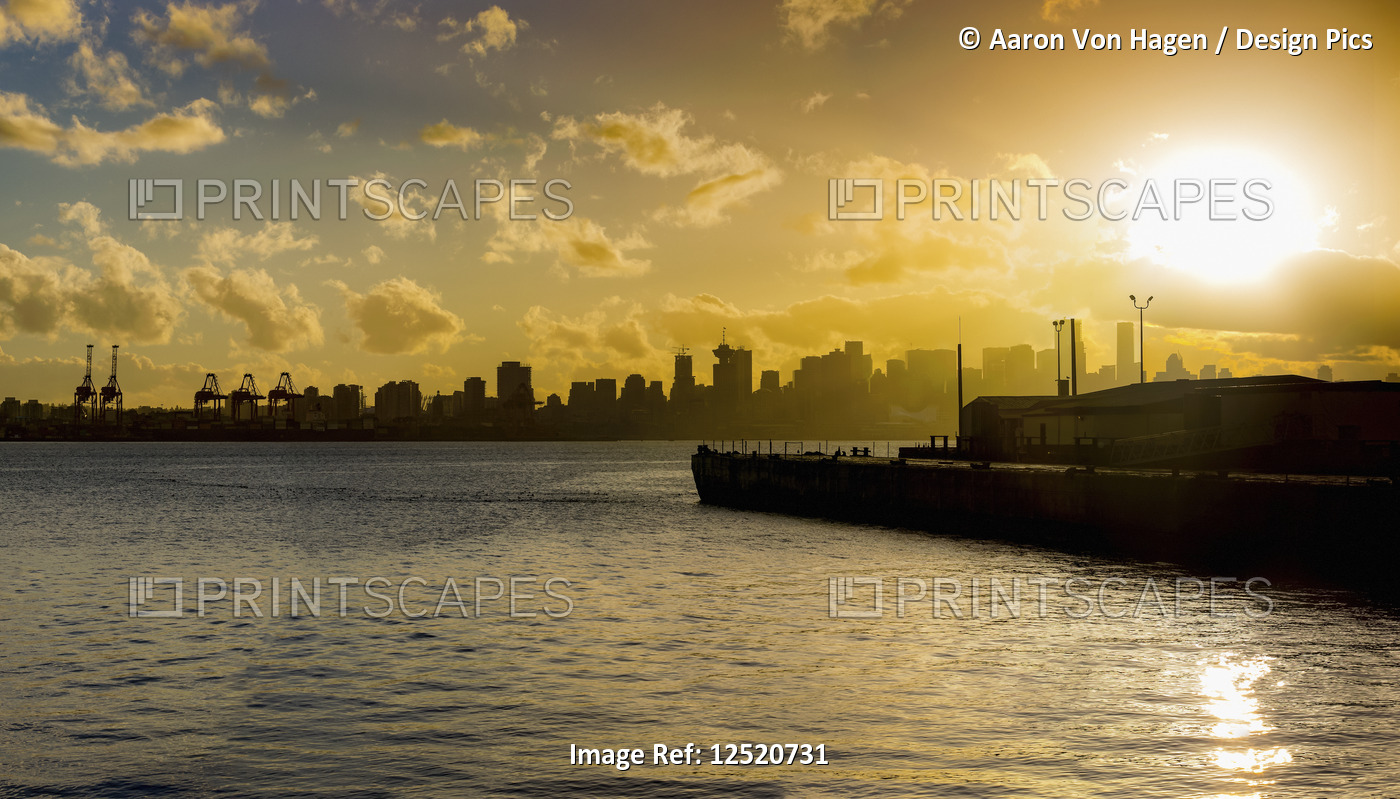Skyline of Vancouver and the coastline with a golden sky at sunrise; Vancouver, ...