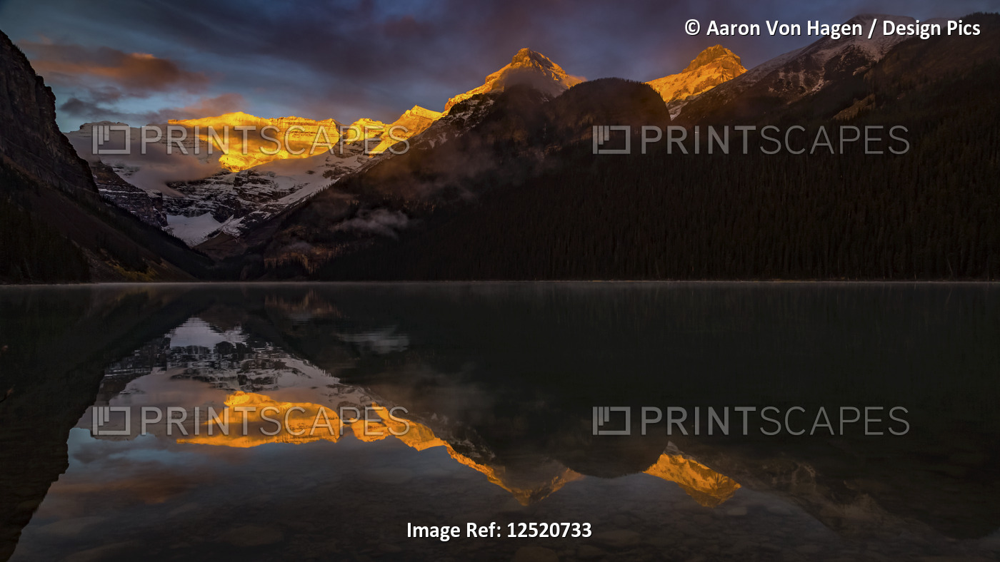 Golden sunlight illuminating the mountain peaks and reflecting in the tranquil ...