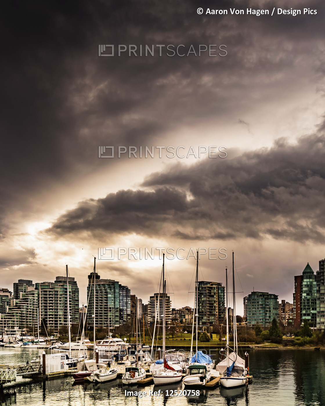Condominium buildings and sailboats moored in the harbour under dark clouds; ...